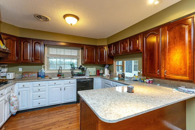 kitchen featuring visible vents, a sink, wood finished floors, a peninsula, and black appliances