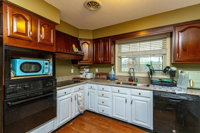 kitchen with visible vents, dark wood-type flooring, black appliances, white cabinetry, and a sink