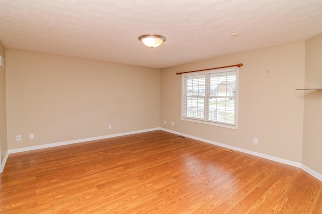 spare room featuring a textured ceiling, baseboards, and wood finished floors