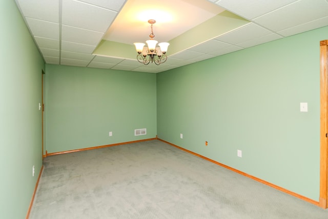 spare room with a drop ceiling, light colored carpet, visible vents, baseboards, and an inviting chandelier