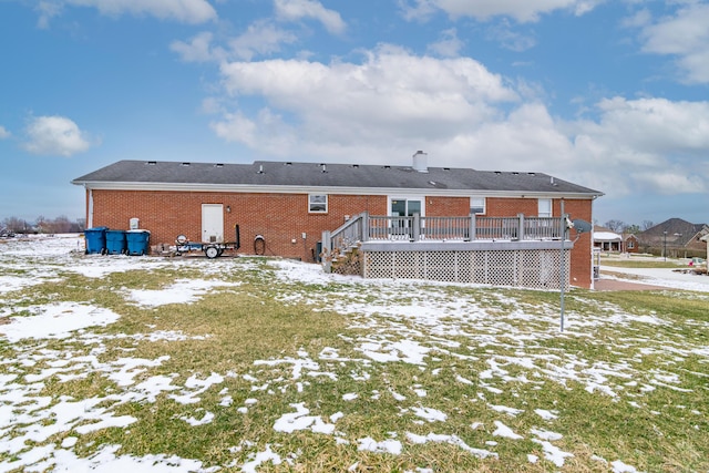 snow covered rear of property featuring brick siding, a chimney, and a wooden deck