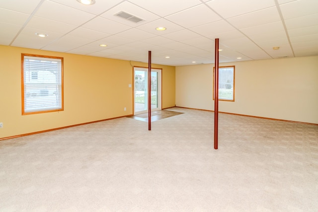 below grade area with visible vents, light carpet, baseboards, and a drop ceiling