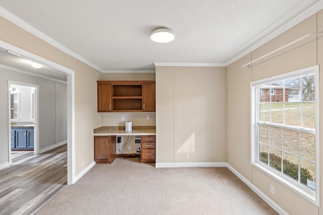 unfurnished office with crown molding, built in desk, a textured ceiling, and a healthy amount of sunlight