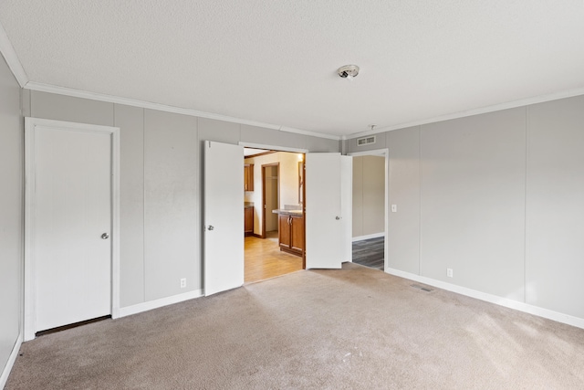 unfurnished bedroom with crown molding, ensuite bath, light colored carpet, and a textured ceiling