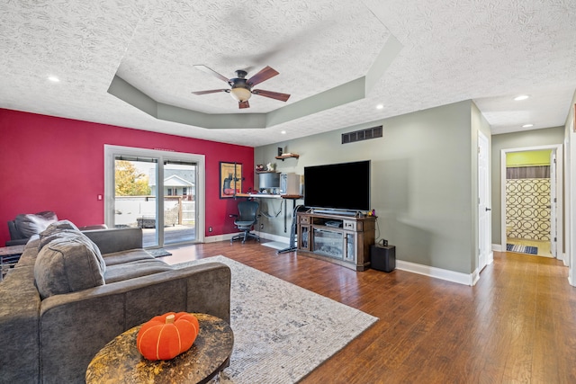 living room featuring ceiling fan, hardwood / wood-style flooring, a raised ceiling, and a textured ceiling