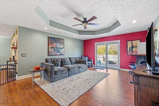 living room featuring a textured ceiling, dark wood-type flooring, a raised ceiling, and ceiling fan