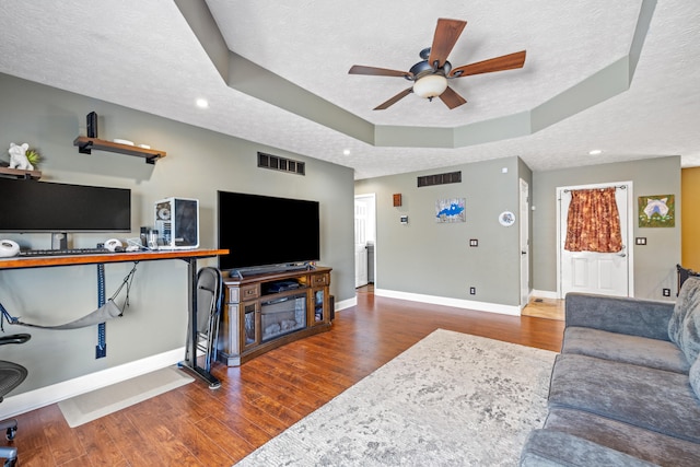 living room with dark hardwood / wood-style flooring, ceiling fan, a tray ceiling, and a textured ceiling