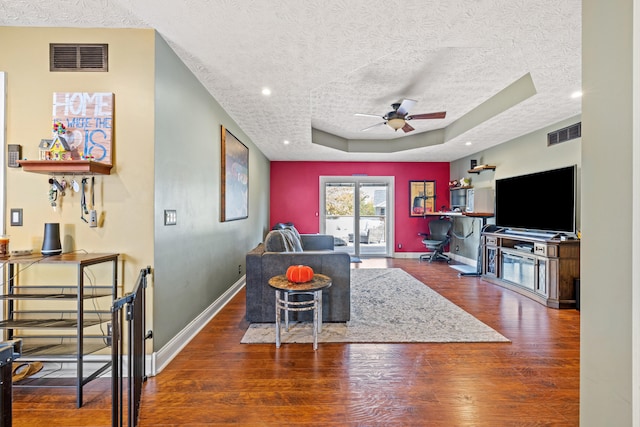 living room with dark hardwood / wood-style flooring, a textured ceiling, a raised ceiling, and ceiling fan