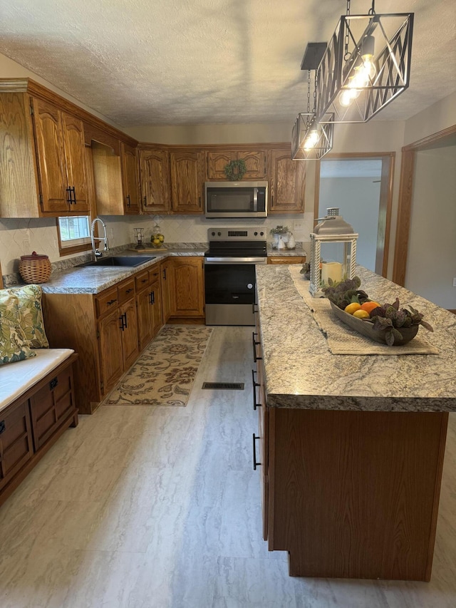 kitchen featuring a kitchen island, decorative light fixtures, sink, stainless steel appliances, and a textured ceiling