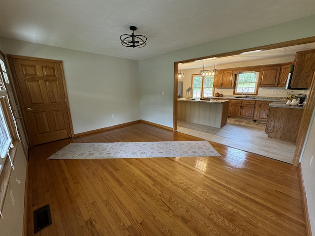 kitchen with decorative light fixtures, kitchen peninsula, sink, and light hardwood / wood-style flooring