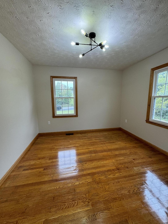 empty room featuring an inviting chandelier, hardwood / wood-style floors, and a textured ceiling