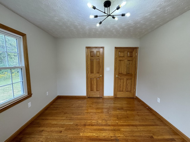 unfurnished room featuring an inviting chandelier, hardwood / wood-style floors, and a textured ceiling