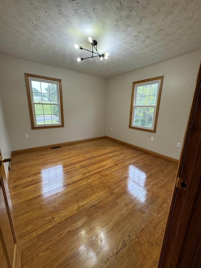 spare room featuring an inviting chandelier, a wealth of natural light, a textured ceiling, and light hardwood / wood-style floors