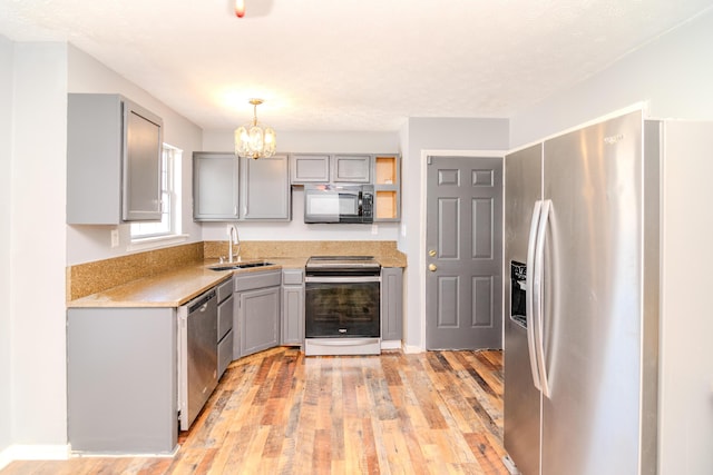 kitchen with light wood-style flooring, gray cabinets, stainless steel appliances, pendant lighting, and a sink