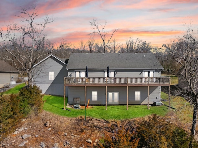 back house at dusk featuring a deck, central AC unit, and a lawn