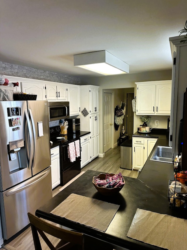 kitchen with appliances with stainless steel finishes, white cabinets, and light hardwood / wood-style flooring