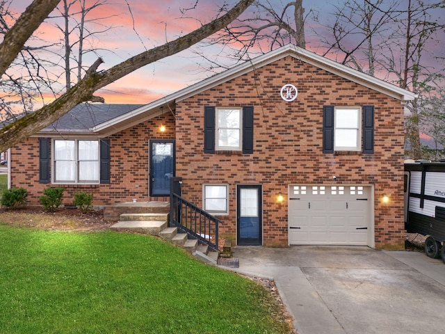 tri-level home with a garage, brick siding, a yard, and driveway