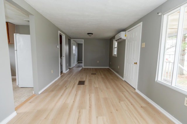 hall with a wall unit AC and light hardwood / wood-style flooring