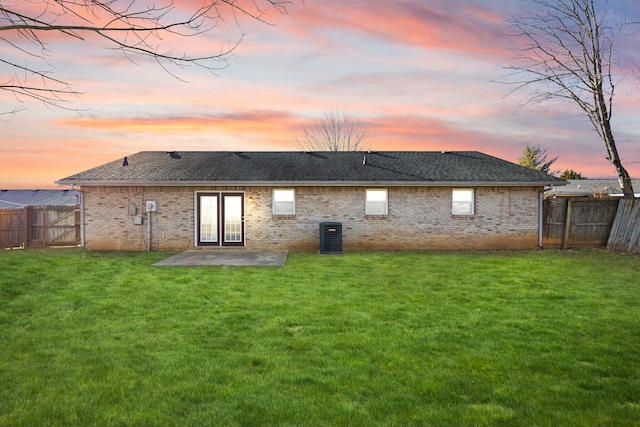 back house at dusk featuring central AC, a patio area, and a lawn