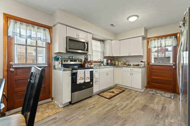 kitchen with light hardwood / wood-style flooring, dark stone counters, white cabinets, and appliances with stainless steel finishes