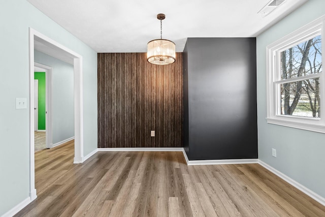 unfurnished dining area with a chandelier, light wood-type flooring, visible vents, and baseboards