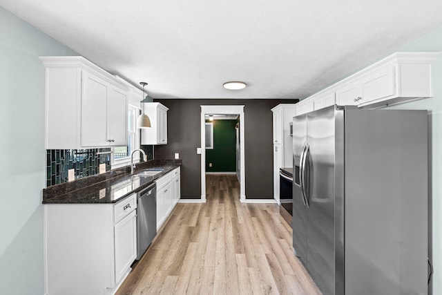 kitchen featuring decorative light fixtures, stainless steel appliances, light wood-style floors, white cabinetry, and a sink