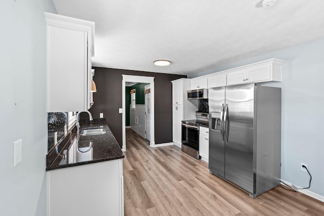 kitchen featuring light wood-style flooring, stainless steel appliances, a sink, white cabinetry, and dark stone countertops