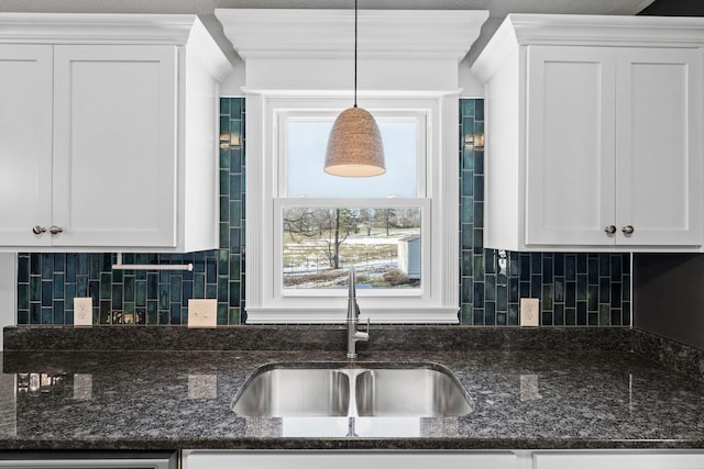 kitchen featuring dark stone countertops, white cabinetry, pendant lighting, and a sink