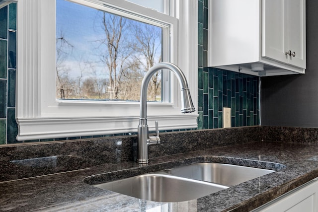 room details featuring dark stone countertops, a sink, and white cabinetry