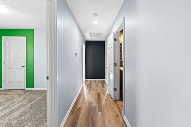 hall with light wood-style floors, visible vents, and baseboards