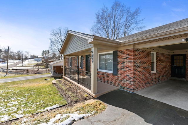 view of side of property with driveway, an attached carport, a lawn, and brick siding