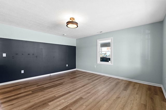 unfurnished room featuring light wood-type flooring, a textured ceiling, and baseboards