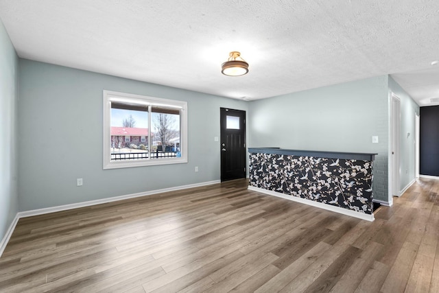 foyer entrance featuring a textured ceiling, baseboards, and wood finished floors