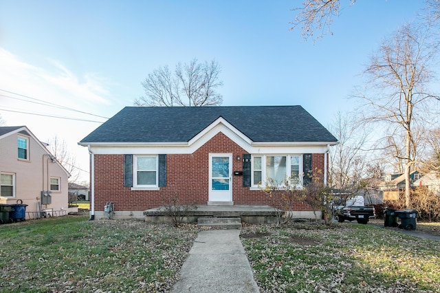 bungalow featuring a shingled roof, a front yard, and brick siding