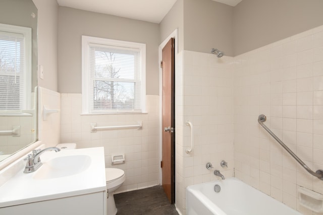 bathroom featuring shower / washtub combination, a wainscoted wall, tile walls, toilet, and vanity