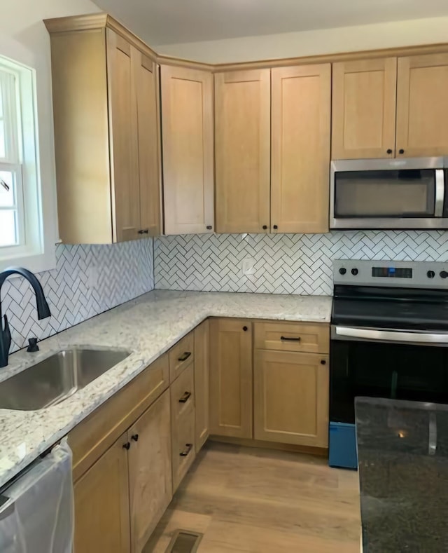 kitchen with light stone counters, light wood-style flooring, a sink, decorative backsplash, and stainless steel appliances