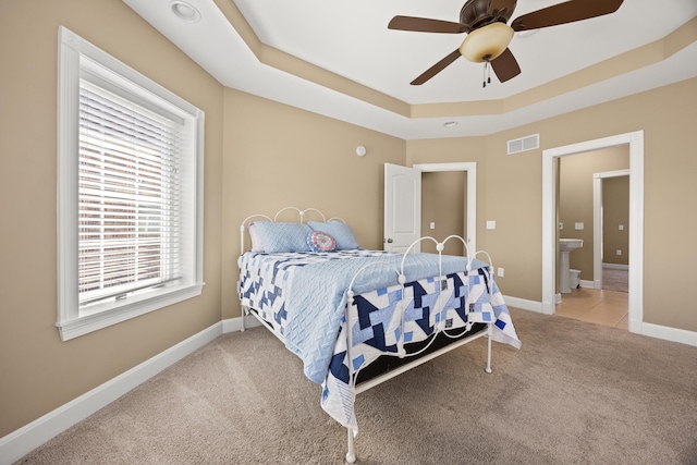 bedroom featuring visible vents, baseboards, light colored carpet, a raised ceiling, and a ceiling fan