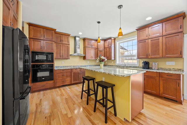 kitchen with light wood finished floors, black appliances, brown cabinets, and wall chimney range hood