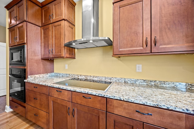 kitchen with light stone countertops, black appliances, wall chimney exhaust hood, and brown cabinetry