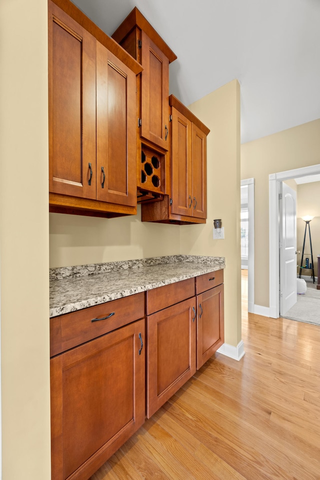 kitchen with baseboards, brown cabinets, light wood-style floors, and light stone countertops