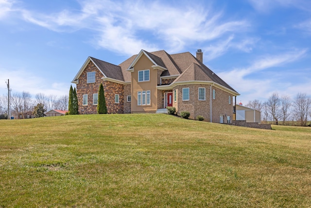 traditional-style house with stone siding, a front yard, and a chimney