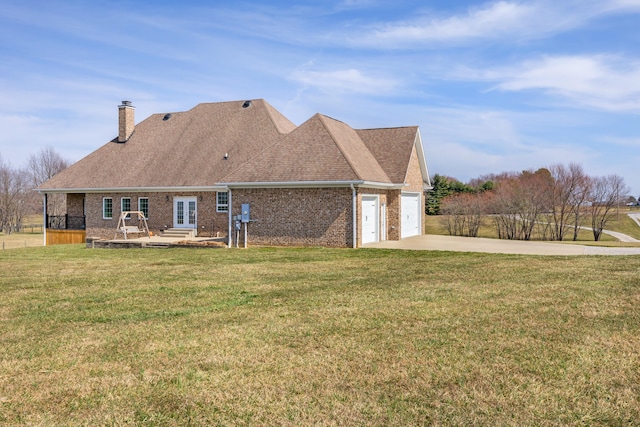 back of property featuring a lawn, driveway, french doors, brick siding, and a chimney