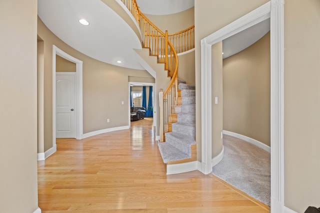 stairs with a towering ceiling, recessed lighting, baseboards, and wood finished floors