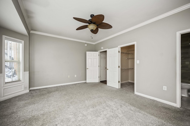 unfurnished bedroom with crown molding, a spacious closet, carpet flooring, and baseboards