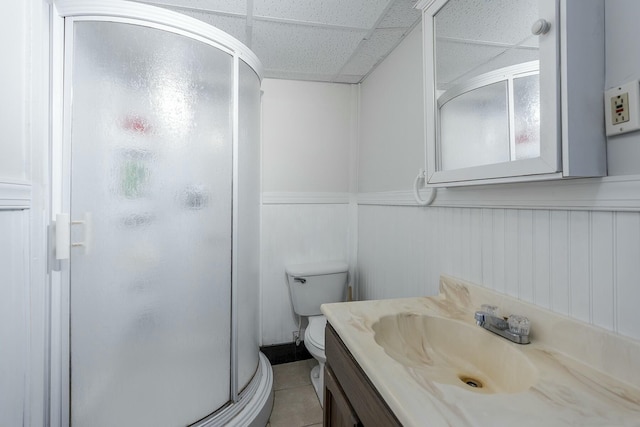 bathroom with a paneled ceiling, a shower with shower door, tile patterned flooring, vanity, and toilet