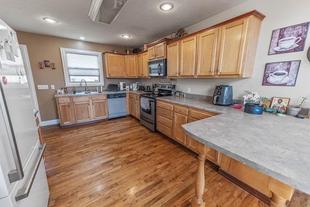 kitchen with stainless steel appliances, a peninsula, a sink, wood finished floors, and light countertops