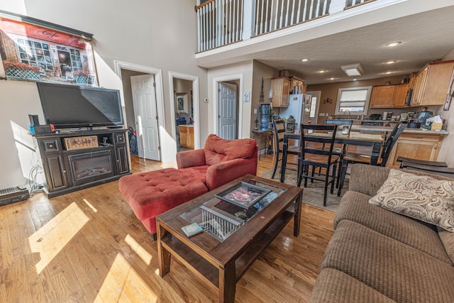 living room featuring a glass covered fireplace, light wood-style flooring, a high ceiling, and recessed lighting