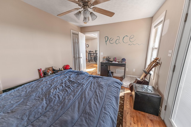 bedroom with a textured ceiling, wood finished floors, visible vents, and a ceiling fan