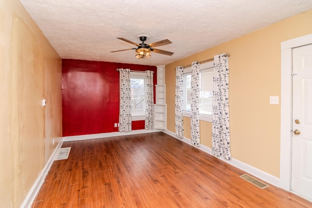 empty room featuring visible vents, a ceiling fan, a textured ceiling, wood finished floors, and baseboards