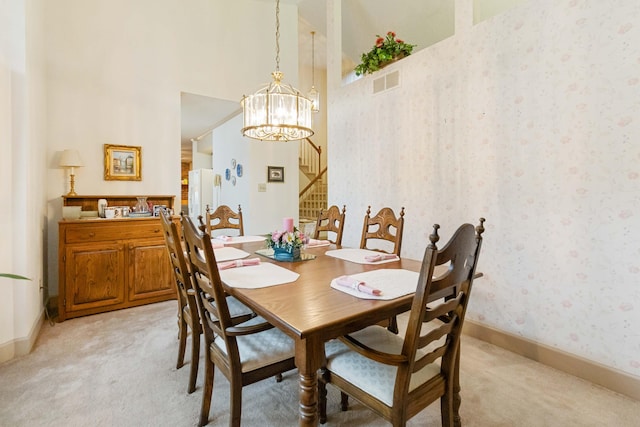 dining area with light carpet, a notable chandelier, and a high ceiling